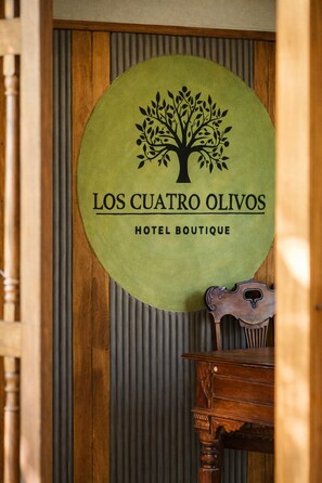 A circular sign with a tree logo and the text 'Los Cuatro Olivos Hotel Boutique' against a wooden background.