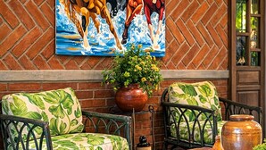 Una habitación con pared de ladrillo carenada, un cuadro grande de un caballo, dos sillones tapizados en verde, una mesa de centro de madera y una planta en maceta.