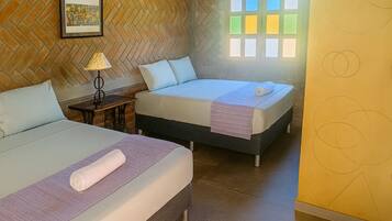Una habitación de hotel con dos camas, un muro de ladrillo con patrón de espiga, un ventanal con vidrios de colores y un cuadro enmarcado en la pared.