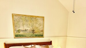 A neatly made bed with a quilt and pillows, a bedside lamp, a floral bench, and a painting on the wall. - 2 bedroom Modern Retreat (Baton Rouge)