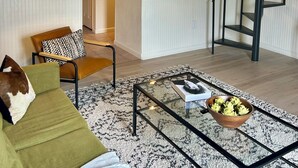 A spacious living area with a high ceiling, a staircase, a sofa, a coffee table, and a view of a kitchen. - 2 bedroom Modern Retreat (Baton Rouge)