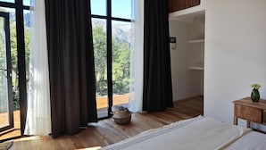 Un dormitorio con una cama grande, vigas de madera, una lámpara colgante, vistas a montañas y suelo de madera.