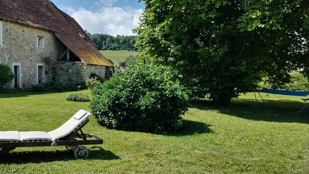 Een stenen huis met een schuin dak, een gazon en een ligstoel.