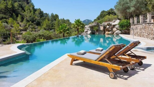 Piscina con sillones de descanso y un muro de piedra.