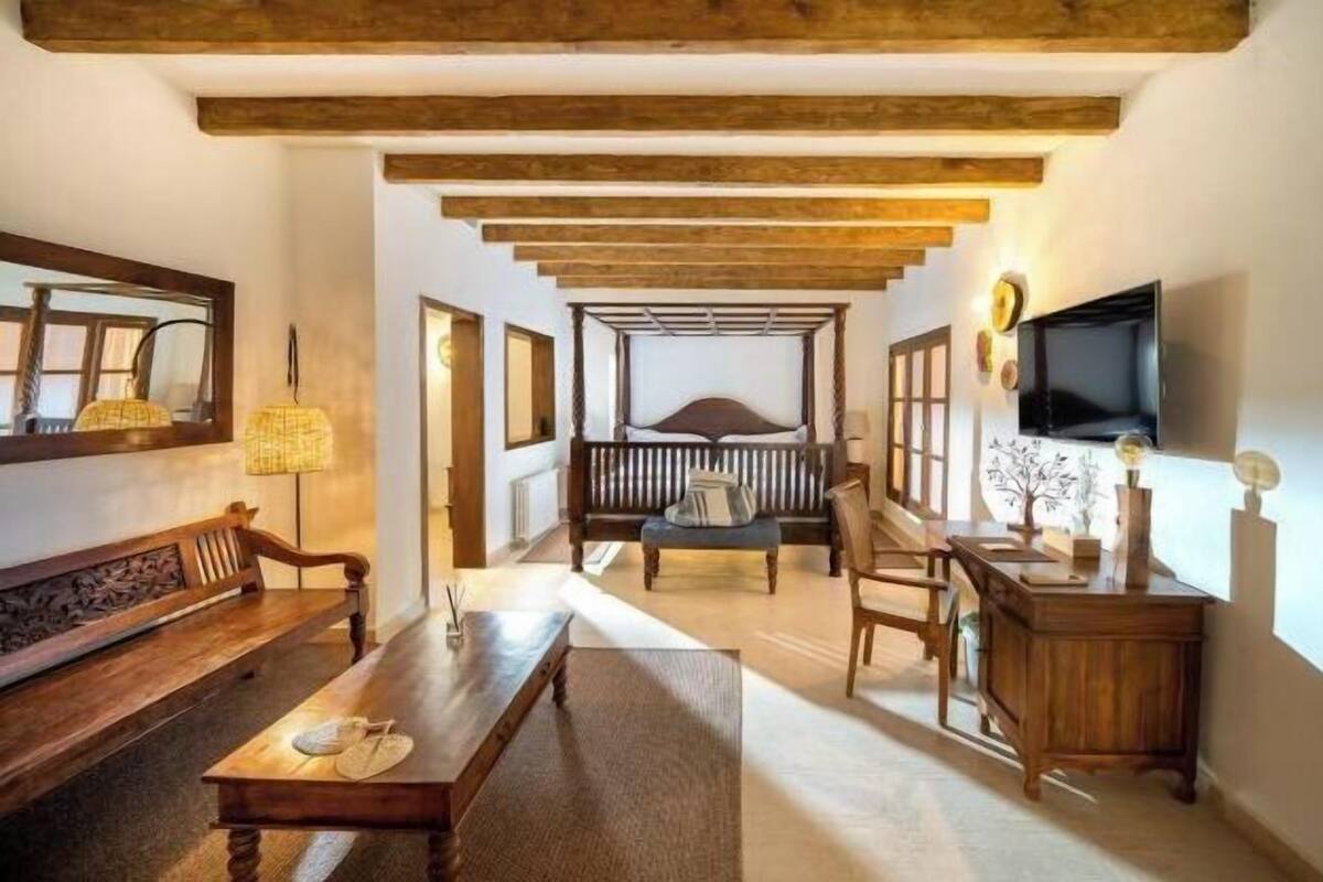 Ein Zimmer mit einer hölzernen Sitzbank, einem Tisch, einem Bett mit Baldachin, einem Fernseher und einem Schreibtisch mit Dekoration.