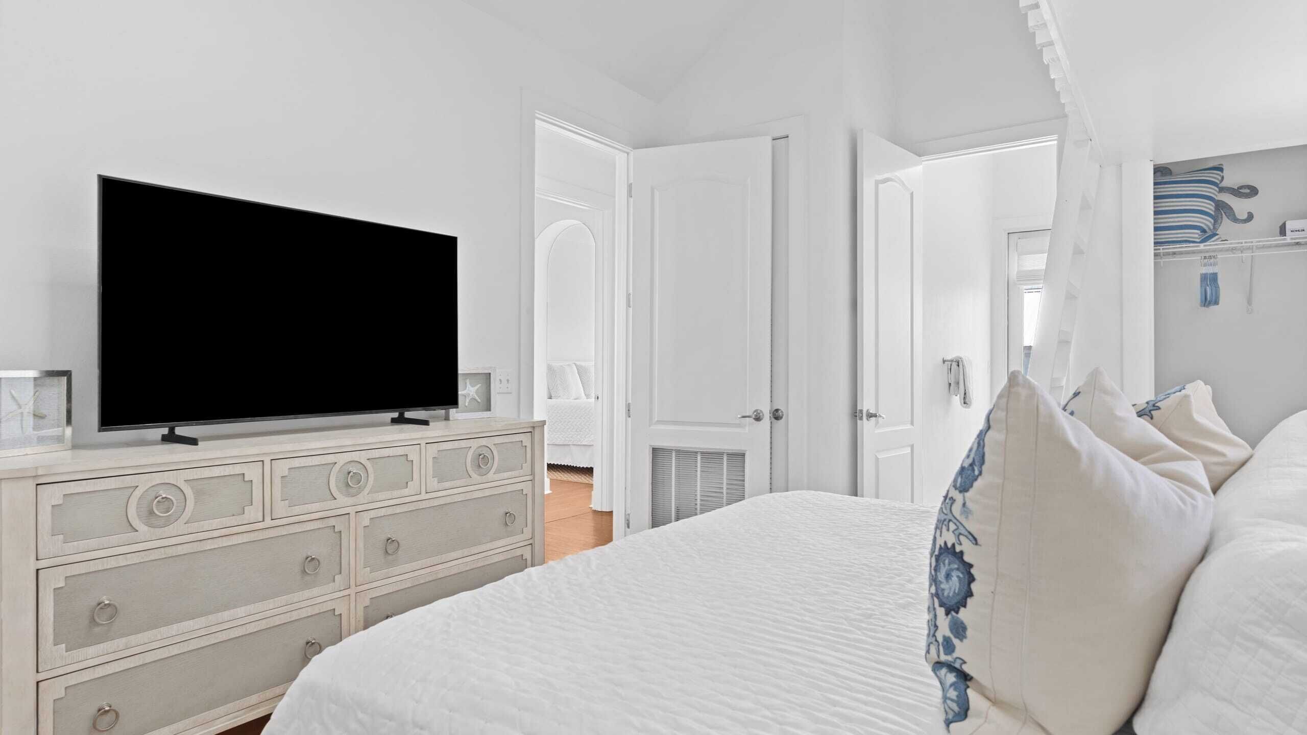 A bedroom with a large bed, a dresser, a television, and an open door leading to another room.
