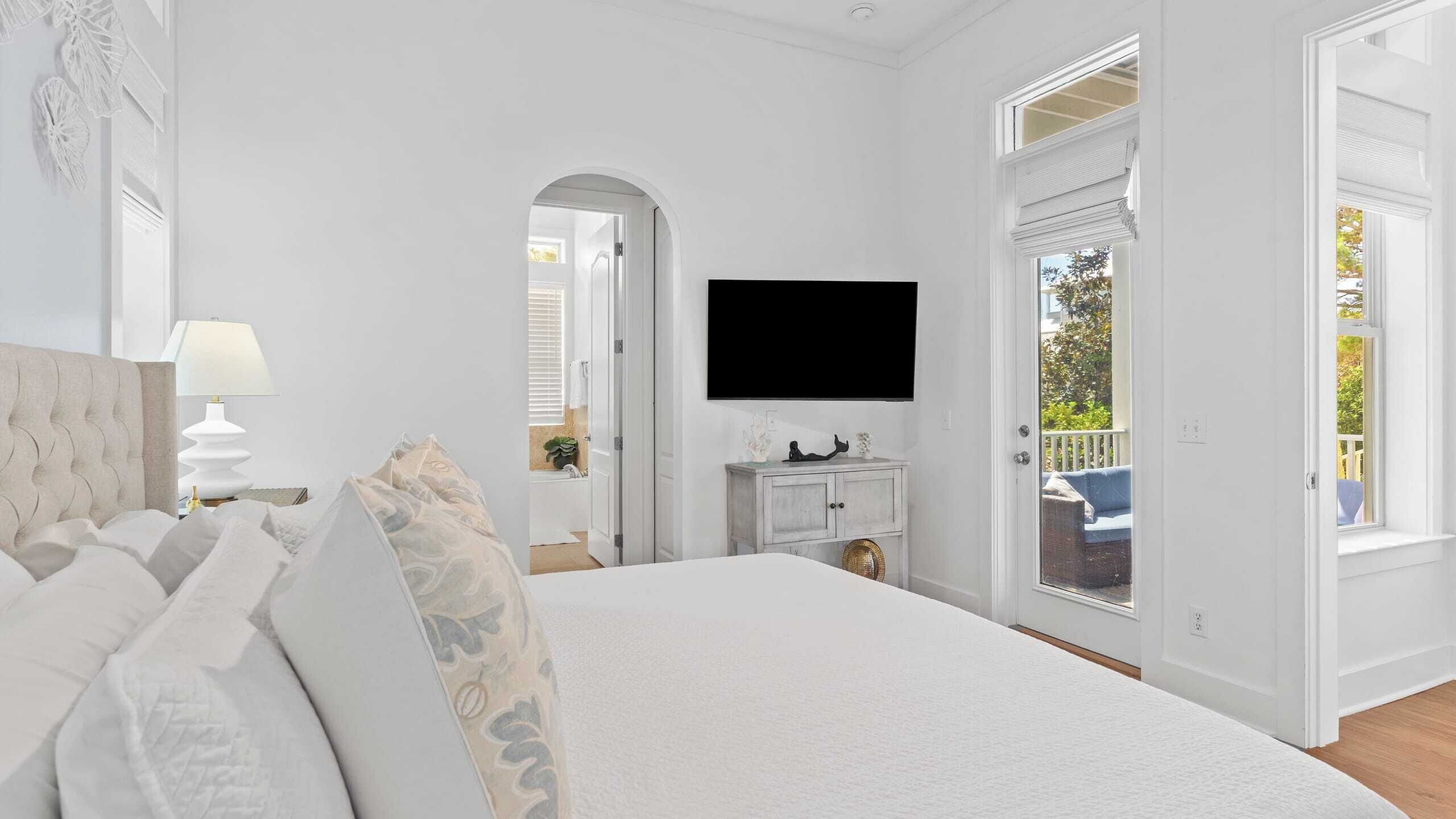 A bedroom with a large bed, a television mounted on the wall, and a view of the outdoors through a door.