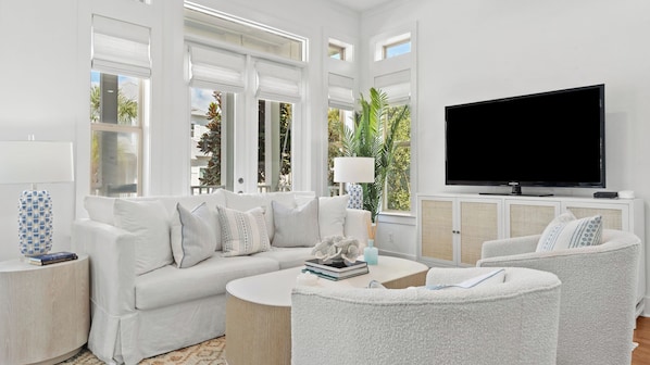 Un salon moderne avec un canapé blanc, deux fauteuils, une table basse et un téléviseur à écran plat.