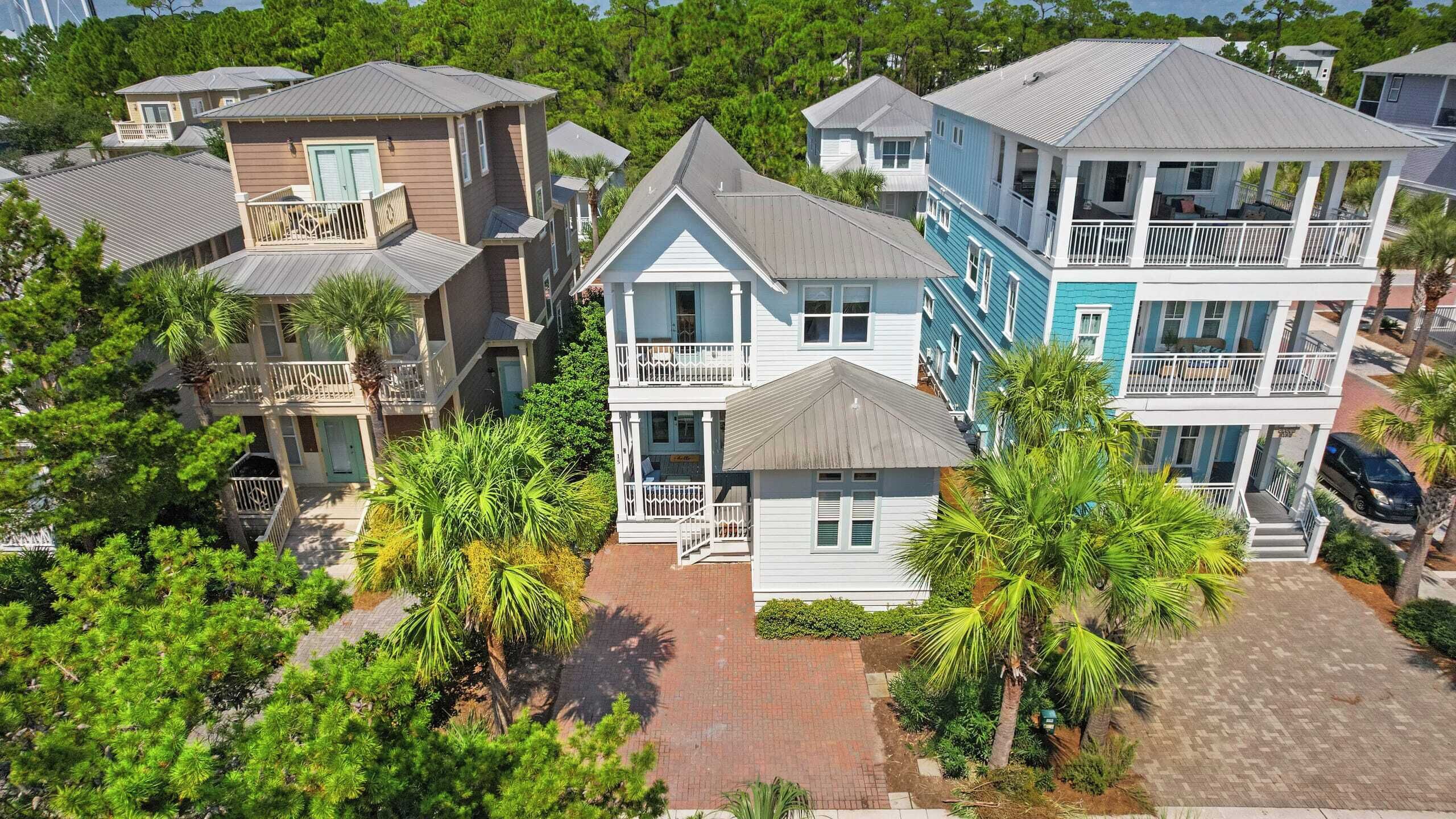 A coastal residential area with multiple two-story houses featuring balconies, some with attached porches, surrounded by lush greenery and palm trees.