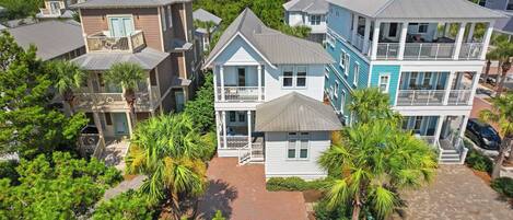 A coastal residential area with multiple two-story houses featuring balconies, some with attached porches, surrounded by lush greenery and palm trees.