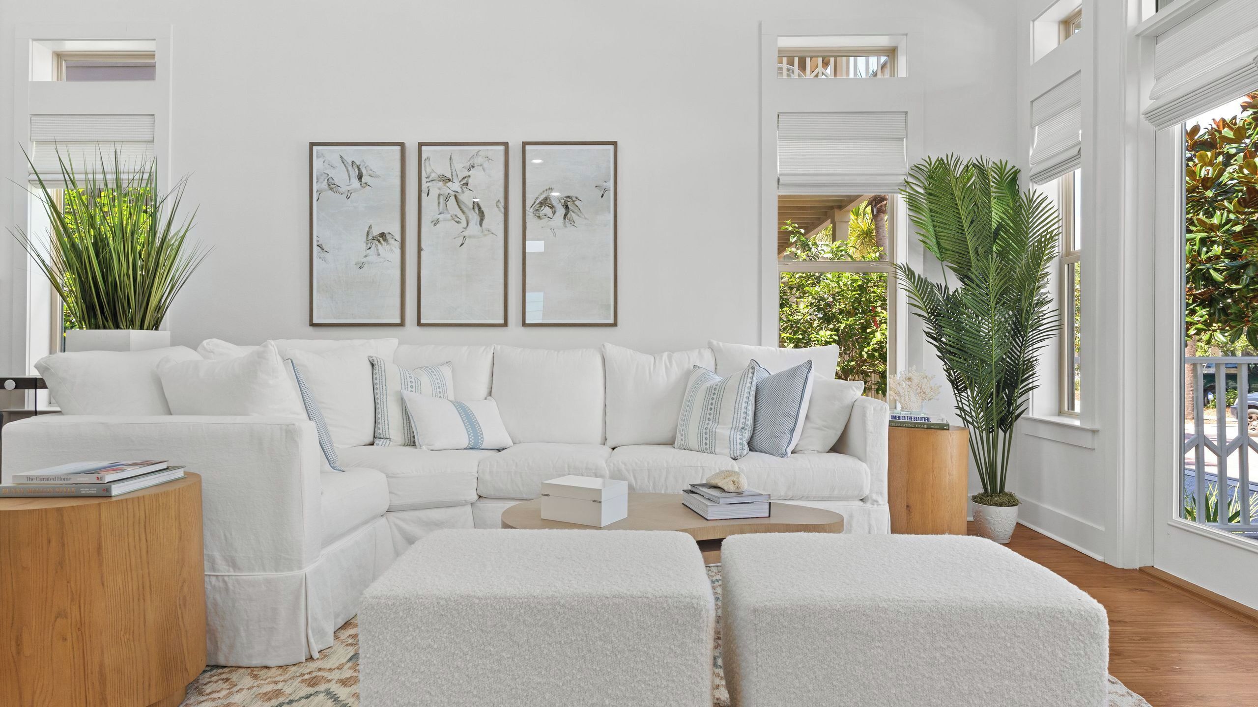 A modern living room with a white sofa, two ottomans, a coffee table, and three framed artworks on the wall.