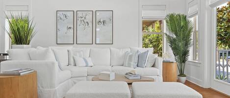 A modern living room with a white sofa, two ottomans, a coffee table, and three framed artworks on the wall.