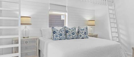 A white bedroom with a bed, two nightstands, a ladder, and a window.