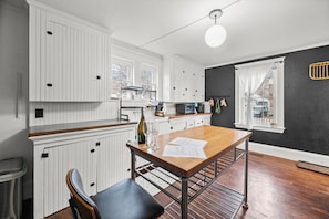 Une cuisine avec des meubles blancs, une table Ă manger en bois et un mur dâaccent noir.