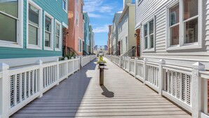 Une promenade en bois dotée de rampes blanches, bordée d’immeubles aux couleurs vives.