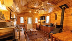Acogedora cabaña con interior de madera, comedor, cocina con estufa y ventilador de techo.