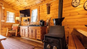 Interior acogedor de una cabaña con paredes de madera, una zona de cocina central, una estufa y un sillón mecedora.