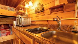 Interior de una cabaña de madera con cocina que incluye una encimera de granito, pileta de acero inoxidable y un tostador.