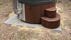 Tinaja de hidromasaje en zona boscosa, con estructura metálica y escalones de madera.