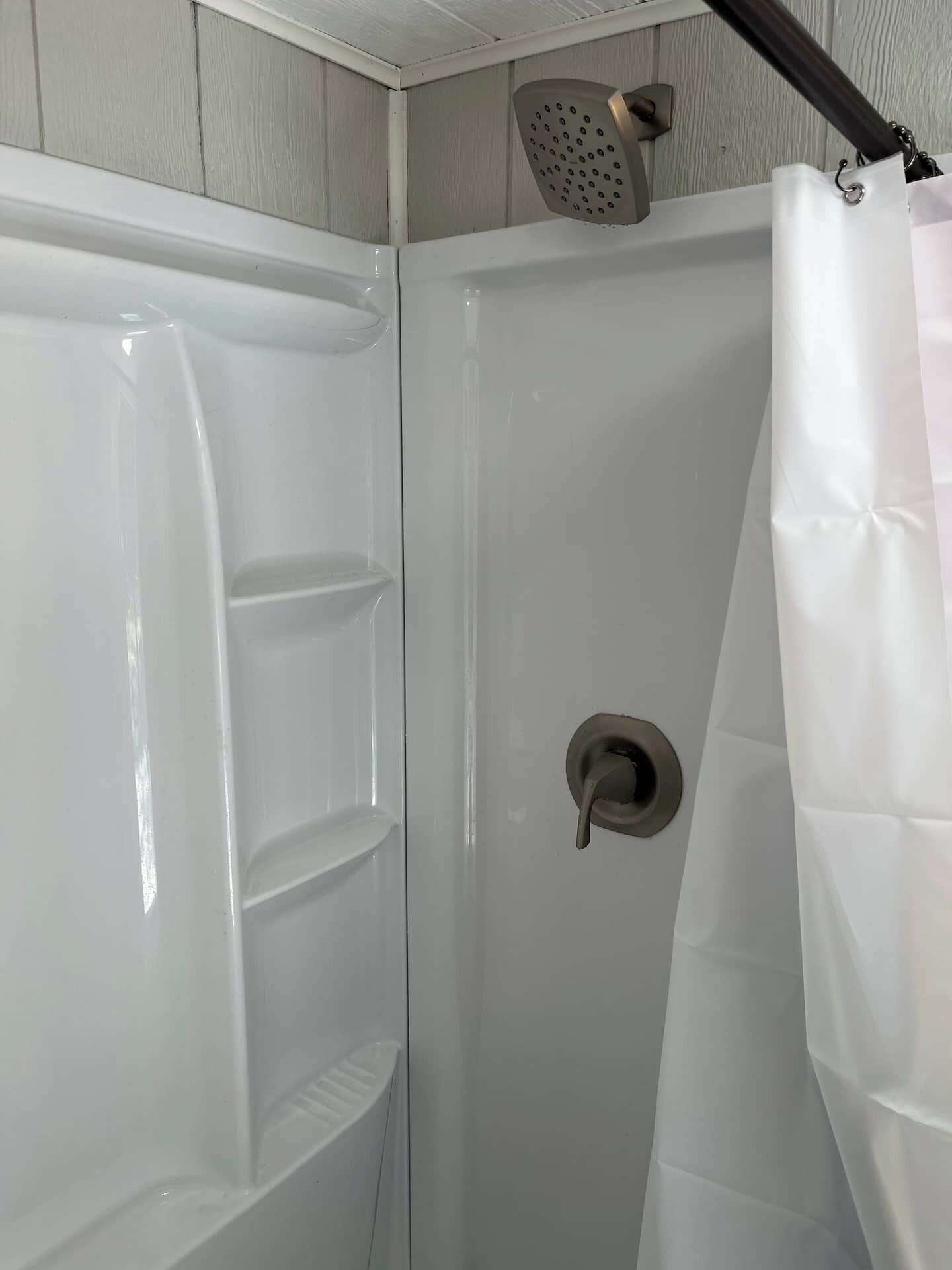 A shower enclosure with a showerhead, a control knob, and a white shower curtain.
