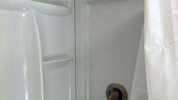 A shower enclosure with a showerhead, a control knob, and a white shower curtain.
