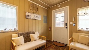 Una habitación acogedora con suelo de madera, un sofá, una silla, una puerta y una ventana con cortinas.