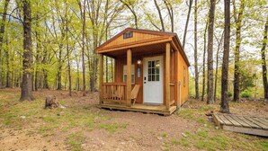 Una pequeña cabaña de madera con un porche, rodeada de árboles.