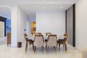 A modern dining area with a rectangular table and six chairs, a trash bin, and a visible staircase in the background.