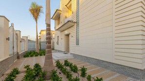 Une cour étroite avec un palmier, un chemin bordé de dalles et un bâtiment à la façade beige.