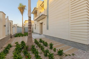 A narrow courtyard with a palm tree, a tiled pathway, and a building with a beige facade.