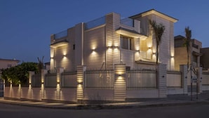 Une maison moderne à deux étages, dotée d’un toit plat, de nombreuses fenêtres et d’une entrée fermée par un portail.