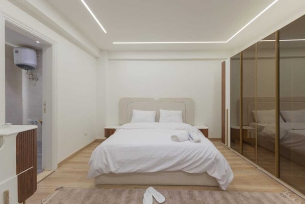 A modern bedroom with a large bed, a walk-in closet, and a bathroom with a shower.