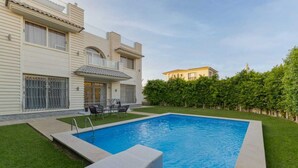 Une piscine avec un espace patio, une petite terrasse et une haie.