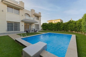 A swimming pool with a patio area, a small deck, and a hedge.