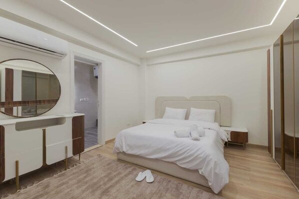 A modern bedroom with a large bed, a bedside table, a mirror, and a wardrobe.