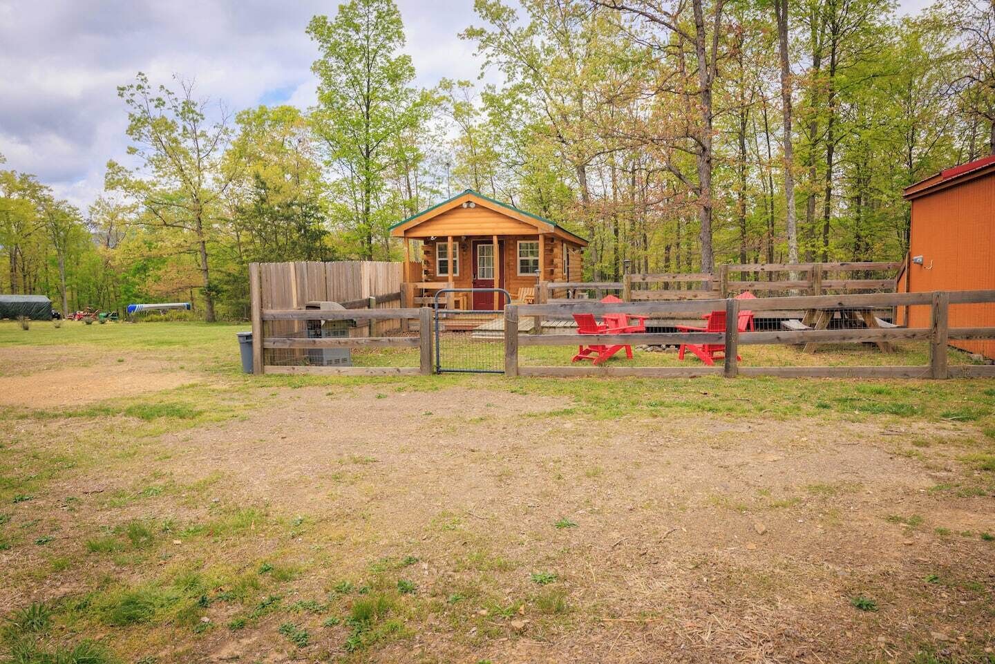 A rustic wooden cabin with a fenced area containing red Adirondack chairs.