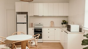 A modern kitchen with white cabinetry, a built-in oven, a microwave, and a dining area with a round table and chairs. - Salt Cottage - charming two–bedroom retreat (Port Fairy)