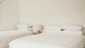 Two single beds with white bedding in a room with a plain white wall and a single bedside lamp. - Salt Cottage - charming two–bedroom retreat (Port Fairy)