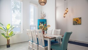 A dining area with a wooden table, white chairs, and a teal chair. There is a blue cabinet with a decorative item on top, a potted plant, and a painting on the wall. - Island Breeze Villa Palm Beach/Noord 7 minutes walking to the nearest beach (Palm Beach/Noord)