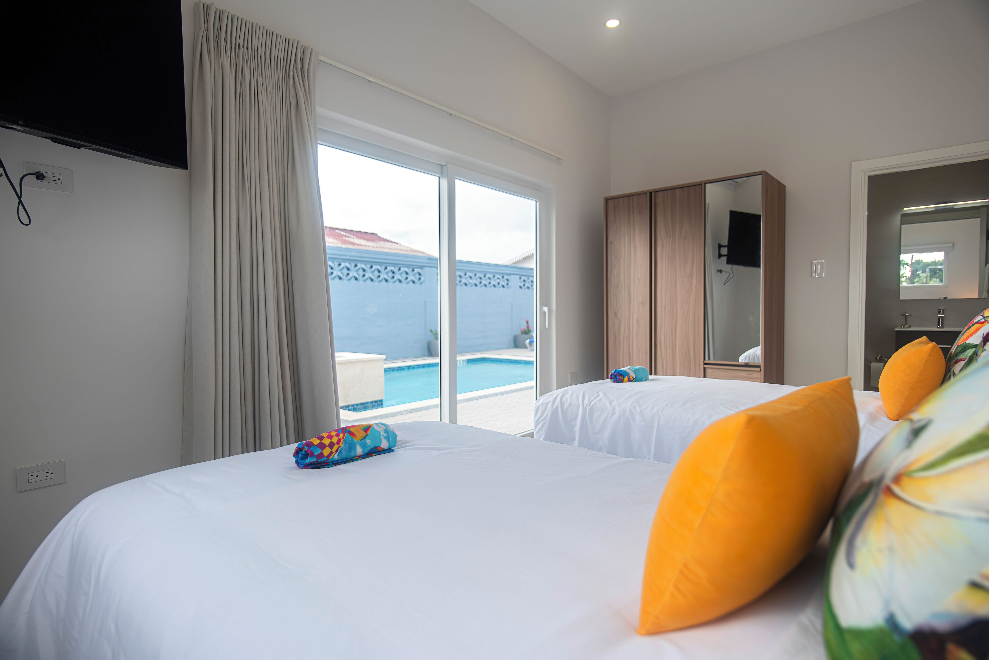 Une chambre d’hôtel avec deux lits, une grande fenêtre avec des rideaux, une télévision et une vue sur une piscine.