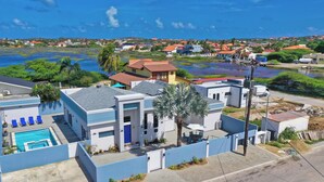 A residential area with a swimming pool, a blue house, and a view of the water. - Island Breeze Villa Palm Beach/Noord 7 minutes walking to the nearest beach (Palm Beach/Noord)
