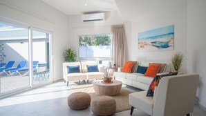 A modern living room with a white sofa, blue chairs, a coffee table, and a painting of a beach scene. - Island Breeze Villa Palm Beach/Noord 7 minutes walking to the nearest beach (Palm Beach/Noord)