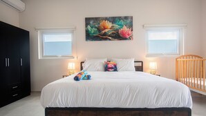 A bedroom with a large bed, two bedside lamps, a crib, and a painting of flowers on the wall. - Island Breeze Villa Palm Beach/Noord 7 minutes walking to the nearest beach (Palm Beach/Noord)