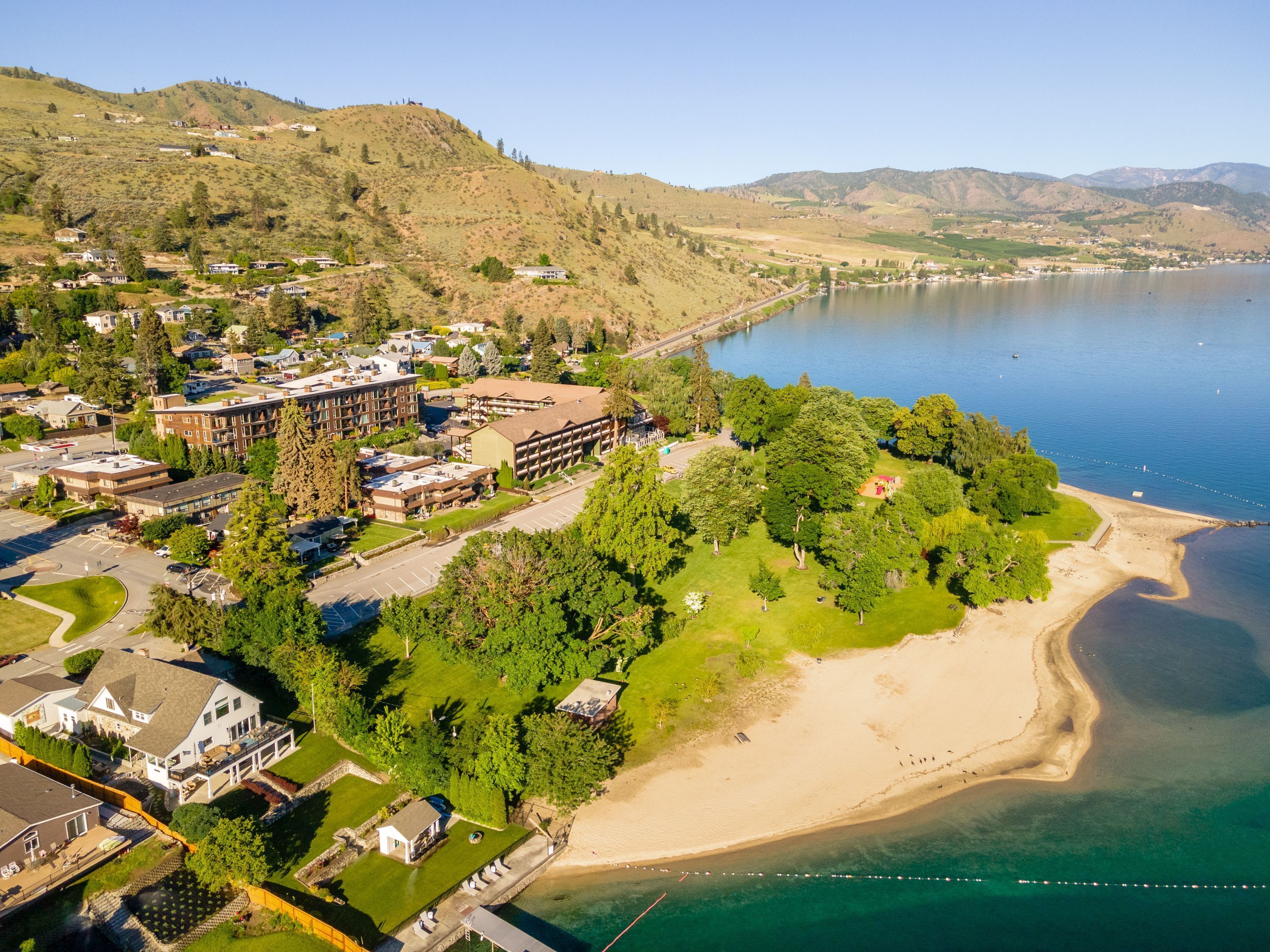 An aerial view of a coastal town with a sandy beach, residential buildings, and a large body of water.