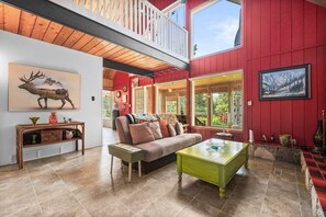 A spacious living area with a high ceiling, a balcony, a large painting of a moose, and a cozy sofa. - The Nest - Retro Cabin w/ Sauna (Rocky View County)