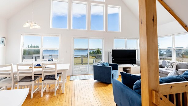 A spacious living room with a large window, a dining area with white furniture, and a cozy seating area with blue cushions.
