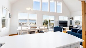 A spacious living area with a large white table, white chairs, a blue sofa, and a TV.