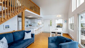 A spacious living area with a blue sofa, a wooden staircase, a kitchen, and a dining area.