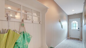 Een gang met een bank, een kapstok met tassen, een deur met een raam en een zeester decoratie aan de muur.