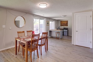 Un comedor con mesa y sillas de madera, una cocina al fondo y una puerta blanca.